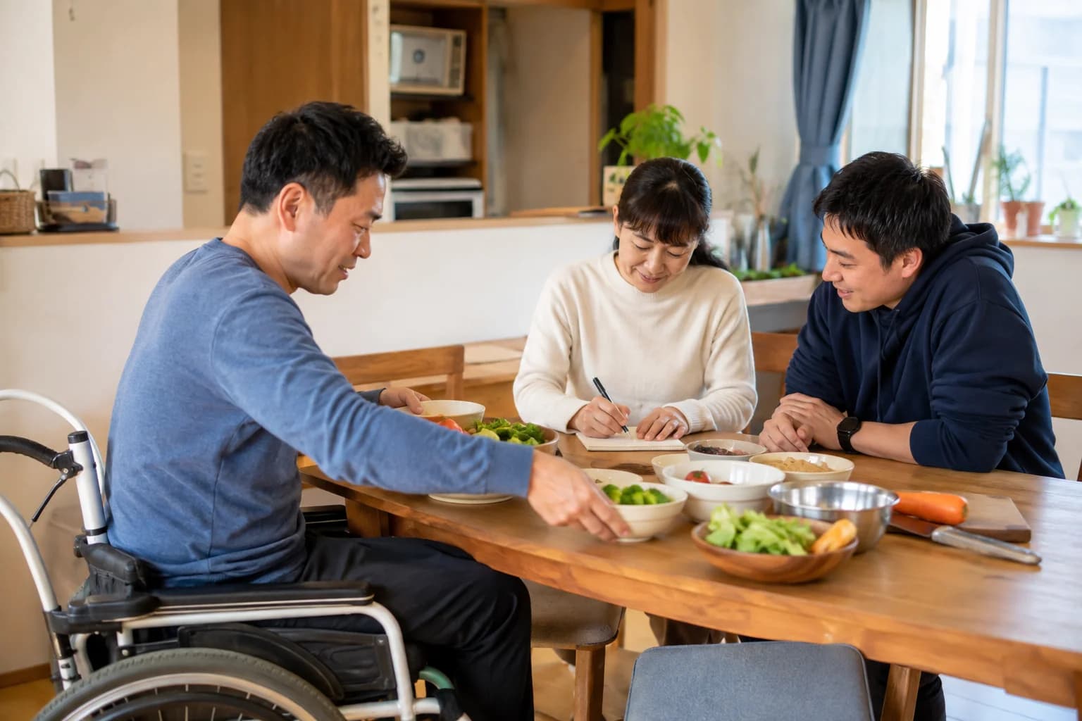 グループホームの食卓に加わる支援員と利用者
